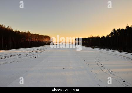 Schneebedecktes Feld zwischen Wäldern am Rand des Rahmens. Winter. Stockfoto