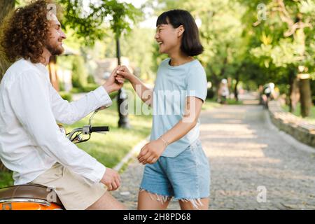 Glückliches junges multiethnisches Paar auf dem Roller genießen sonnigen Tag im Park Stockfoto