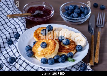 Hüttenkäse-Pfannkuchen, Pfannkuchen mit Quark, Syrniki mit frischen Beeren und Banane, Marmelade, Sauerrahm zum Frühstück. Selektiver Fokus. Stockfoto