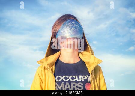 17. Juni 2021, Sankt Petersburg, Russland. Frau im gelben Regenmantel in Spiegelbrille mit Himmelsreflexion und T-Shirt mit „Occupy Mars“-Schriftzug. Stockfoto