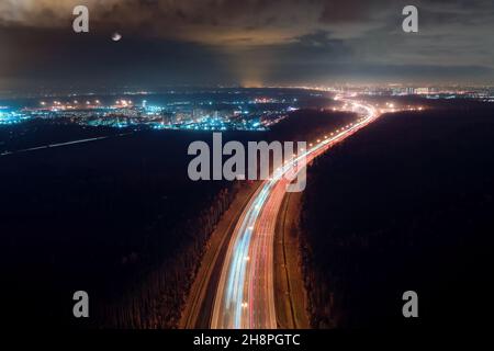 Highway Road und beleuchtete Stadt bei Nacht. Industrielle Luftlandschaft bei Mondlicht, Langzeitbelichtung Stockfoto