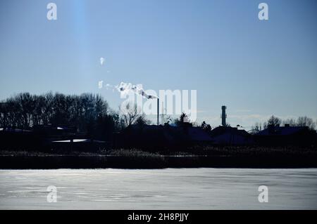 Rauchende Kamine und Dächer von Mehrfamilienhäusern an einem Wintertag gegen die aufgehende Sonne. Winter. Stockfoto