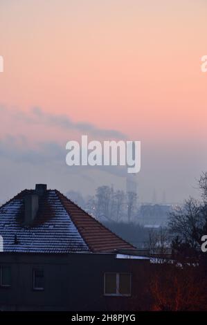 Rauchende Kamine und Dächer von Mehrfamilienhäusern an einem Wintertag gegen die aufgehende Sonne. Winter. Stockfoto