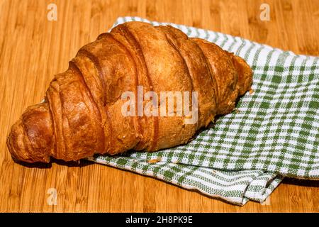 Nahaufnahme eines Croissants auf einem karierten Küchentuch auf einem Holztisch Stockfoto
