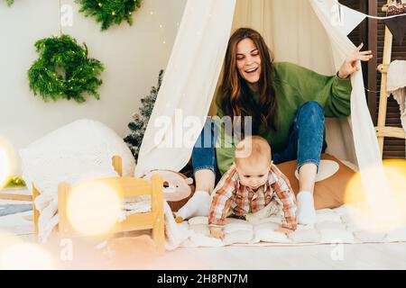 Lachend glücklich junge rothaarige Mutter spielt mit aktiven Kleinkind im Zelt im Kinderzimmer. Familienspaß, Glück aus Zeitvertreib mit Kindern. Stockfoto