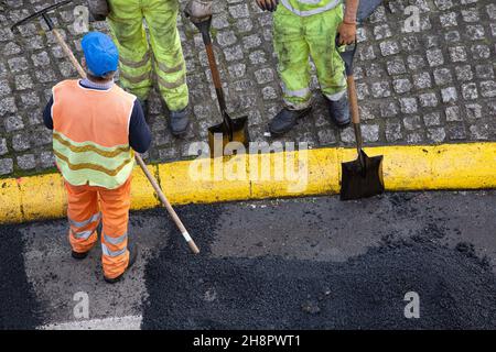 Nicht erkennbare Bauarbeiter während der Asphalting Road-Arbeiten auf der Stadtstraße. Asphaltbelag. High-Angle-Ansicht Stockfoto