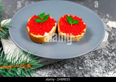 Die Sandwiches mit dem roten Kaviar auf der grauen Platte auf dem Tisch mit den Zweigen des Weihnachtsbaums. Weihnachten, Neujahr. Festliche Speisen. Stockfoto