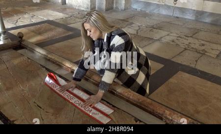 Jerusalem, Israel. 1st Dez 2021. Miss Canada Tamara Jemuovic kniet im Gebet über dem Stein der Salbung oder dem Stein der Unktion in der Grabeskirche, als Teilnehmer des Miss Universe-Festzugs am 01. Dezember 2021 in Jerusalem, Israel, die Altstadt bereisen. Der Miss Universe Wettbewerb 70th wird trotz Reisebeschränkungen aufgrund der Omicron-Coronavirus-Variante im israelischen Ferienort Eilat am Roten Meer stattfinden. Kredit: Eddie Gerald/Alamy Live Nachrichten Stockfoto