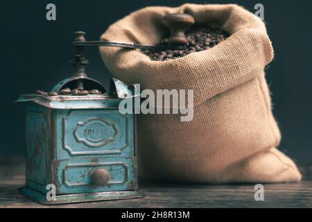 Horizontale Detail gerade Studio-Aufnahme von Stillleben mit vintage manuelle grüne Metall Kaffeemühle, Jute-Tasche und Kaffeebohnen auf alten Holztisch Stockfoto