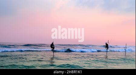 Silhouetten der traditionellen Stelzenfischer bei Sonnenuntergang in der Nähe von Galle in Sri Lanka. Breites Foto . Stockfoto