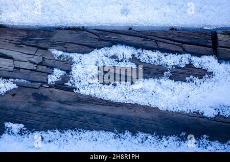 Textur einer grauen Holzdiele, die in Eis verkettet ist. Winterhintergrund. Ein Brett mit Schneeflocken und einem eisigen Rahmen um es herum. Zerstörung und Alterung Konzept Stockfoto