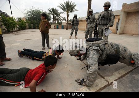 090408-A-5493S-392 US Army Staff Sgt. Josh Hedetniemi macht am 8. April 2009 Liegestütze, um irakische Kinder vor einer Schule in der Nähe von Sheik Hammad, Irak, zu unterhalten. Hedetniemi ist von Alpha Company, 1st Bataillon, 111th Infanterie-Regiment, 56th Stryker Brigade Combat Team, 28th Infanterie-Division. DoD-Foto von Sgt. Jacob H. Smith, U.S. Army. (Freigegeben) Stockfoto