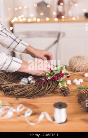 Frau Handwerker machen Weihnachtsfeiertagskranz auf einem Tisch unter durch Neujahrsdekor. Frauenhobby. Vorbereitungen für das Urlaubskonzept. Weihnachten wr Stockfoto