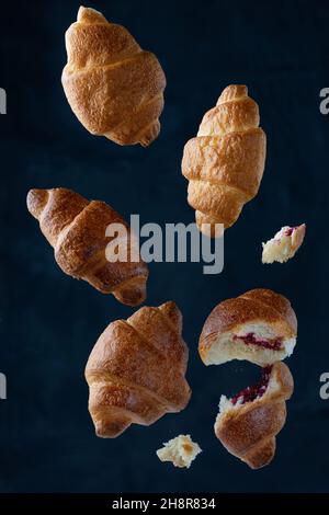 Fallende leckere frisch gebackene Croissants auf blauem Hintergrund Stockfoto