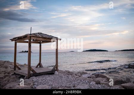 Wunderschöner, friedlicher Sonnenuntergang über einem Holzpavillon am Strand ohne Menschen in der Szene Stockfoto