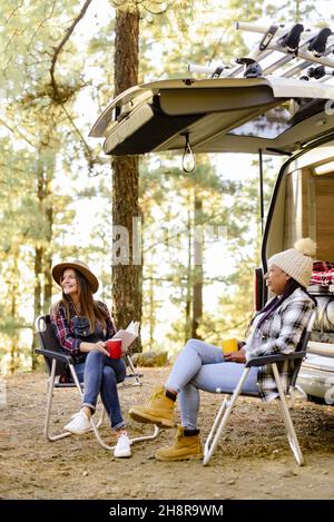 Verschiedene Reisende Frauen in der Nähe Wohnmobil in Wäldern Stockfoto