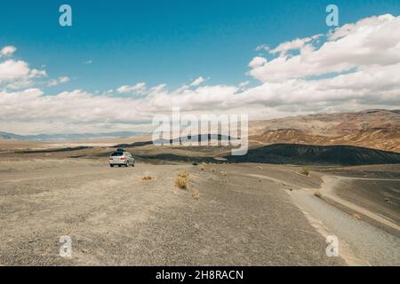 Ausflug zum Death Valley National Park. Wüstenlandschaft und ein Auto auf einer unbefestigten Straße, wolkiger Himmel im Hintergrund Stockfoto