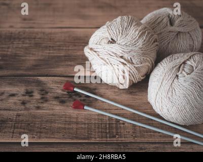 Garn und Nadeln zum Stricken, Nahaufnahme. Fadenkugeln und Stricknadeln auf Holzhintergrund Stockfoto