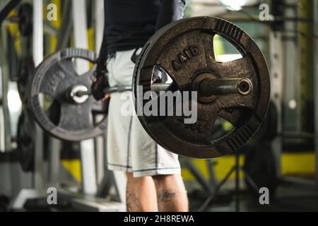 Seitenansicht eines unbekannten kaukasischen Mannes, der Hantelgewichtsgriff an Gewichten im Fitnessstudio hält, wenn er in der Totzugposition im Mittelteil des Fitnessraums den Kopierraum trainiert Stockfoto