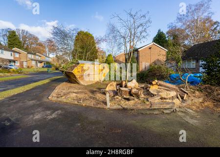 Eine große rostende, zerrüttete abfallentsorgung voller Äste und Gartenabfälle befindet sich im Vorgarten einer Straße in Surrey, Südostengland Stockfoto