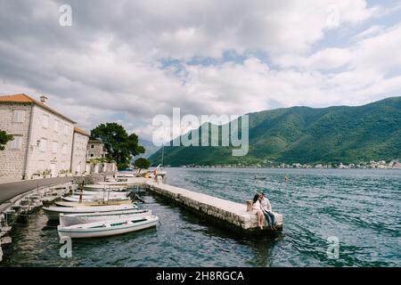 Mann und Frau sitzen auf dem Pier am Wasser neben den festsitzenden Booten Stockfoto