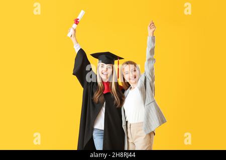 Glückliche weibliche Abschlussstudentin mit ihrer Mutter auf farbigem Hintergrund Stockfoto