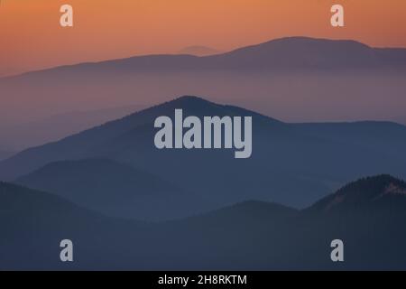 Ein nebliger und rauchiger Sonnenaufgang aus den kanadischen Rockies. Schichten von Farben mit Schichten von Bergkappen, die durch Nebel und Rauch ragen. Stockfoto