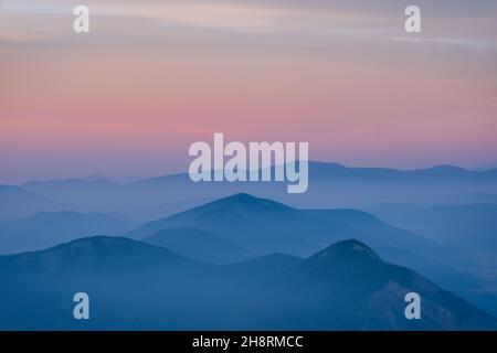 Ein nebliger und rauchiger Sonnenaufgang aus den kanadischen Rockies. Schichten von Farben mit Schichten von Bergkappen, die durch Nebel und Rauch ragen. Stockfoto