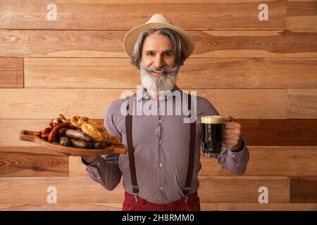 Gutaussehender Mann in traditioneller deutscher Kleidung, mit Bier und Snacks auf Holzhintergrund Stockfoto
