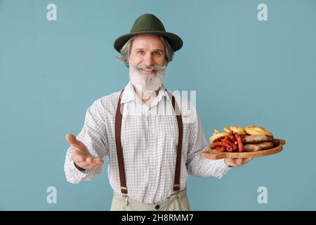 Schöner älterer Mann in traditioneller deutscher Kleidung und mit Snacks auf farbigem Hintergrund Stockfoto