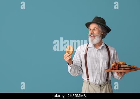 Schöner älterer Mann in traditioneller deutscher Kleidung und mit Snacks auf farbigem Hintergrund Stockfoto