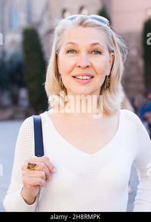 Porträt einer reifen fröhlichen Frau in weißer Bluse auf einer alten Stadtstraße stehen Stockfoto