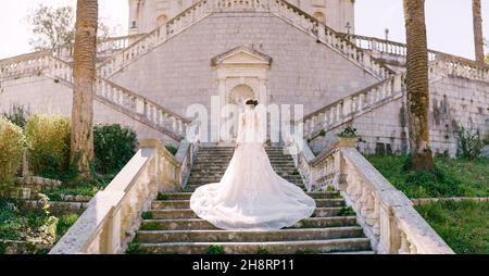 Braut in weißem Kleid steht auf Steintreppen in einem grünen Garten Stockfoto