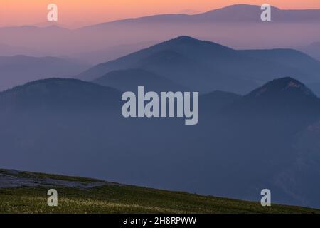 Ein nebliger und rauchiger Sonnenaufgang aus den kanadischen Rockies. Schichten von Farben mit Schichten von Bergkappen, die durch Nebel und Rauch ragen. Stockfoto