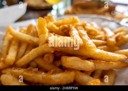 Nahaufnahme von zerfetzten und frittierten, goldenen pommes Frites in einem Korb, der mit weißem Papier ausgekleidet ist, an einem Restauranttisch Stockfoto