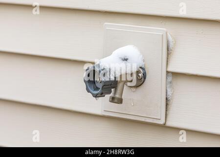 Im Winter ist der Wasserzapfen im Freien mit Schnee bedeckt. Hausreparatur, Wartung und Wetterschutzkonzept Stockfoto
