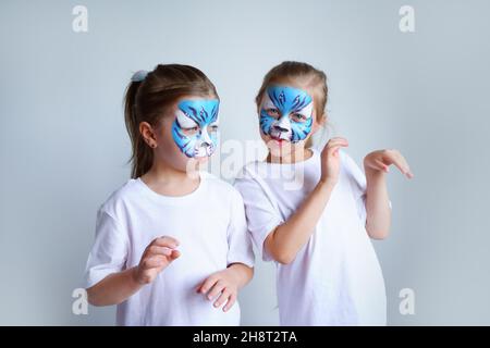 Zwei Schwesternmädchen mit Aqua-Make-up in Form eines blauen WasserTierkreiszeichens zeigen einen Tiger auf weißem Hintergrund, ein konzeptionelles Symbol des neuen 2022 Stockfoto