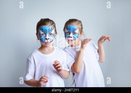 Zwei Schwesternmädchen mit Aqua-Make-up in Form eines blauen WasserTierkreiszeichens zeigen einen Tiger auf weißem Hintergrund, ein konzeptionelles Symbol des neuen 2022 Stockfoto