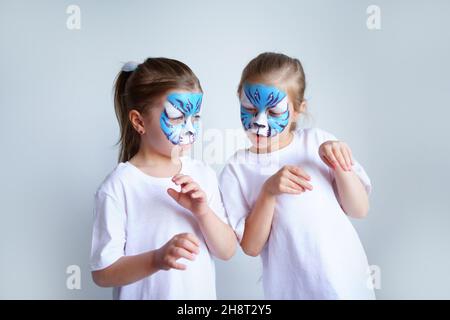 Zwei Schwesternmädchen mit Aqua-Make-up in Form eines blauen WasserTierkreiszeichens zeigen einen Tiger auf weißem Hintergrund, ein konzeptionelles Symbol des neuen 2022 Stockfoto