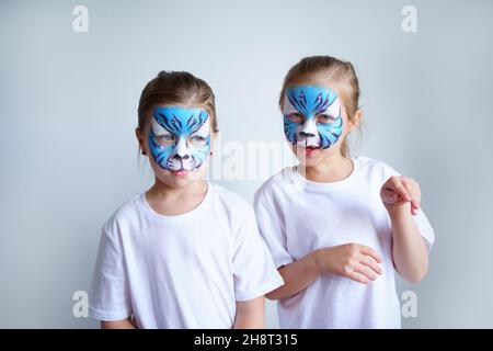 Zwei Schwesternmädchen mit Aqua-Make-up in Form eines blauen WasserTierkreiszeichens zeigen einen Tiger auf weißem Hintergrund, ein konzeptionelles Symbol des neuen 2022 Stockfoto