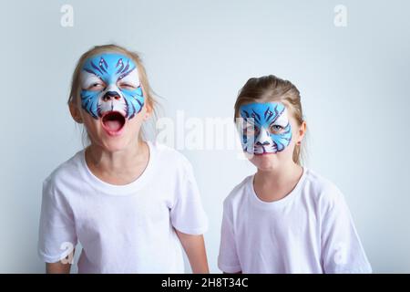 Zwei Schwesternmädchen mit Aqua-Make-up in Form eines blauen WasserTierkreiszeichens zeigen einen Tiger auf weißem Hintergrund, ein konzeptionelles Symbol des neuen 2022 Stockfoto