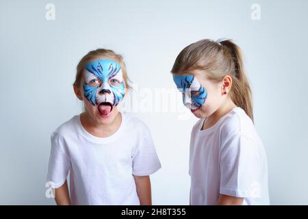 Zwei Schwesternmädchen mit Aqua-Make-up in Form eines blauen WasserTierkreiszeichens zeigen einen Tiger auf weißem Hintergrund, ein konzeptionelles Symbol des neuen 2022 Stockfoto