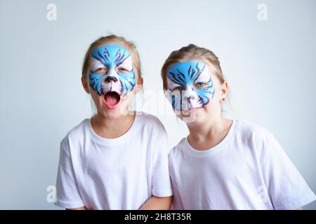 Zwei Schwesternmädchen mit Aqua-Make-up in Form eines blauen WasserTierkreiszeichens zeigen einen Tiger auf weißem Hintergrund, ein konzeptionelles Symbol des neuen 2022 Stockfoto