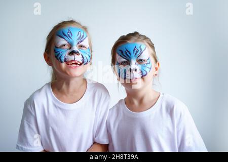 Zwei Schwesternmädchen mit Aqua-Make-up in Form eines blauen WasserTierkreiszeichens zeigen einen Tiger auf weißem Hintergrund, ein konzeptionelles Symbol des neuen 2022 Stockfoto