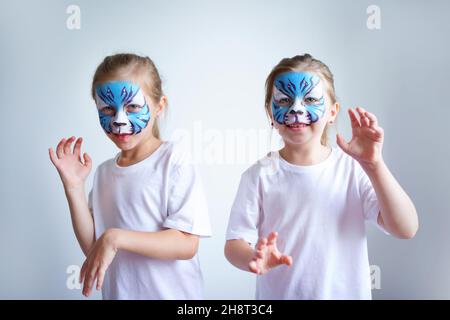 Zwei Schwesternmädchen mit Aqua-Make-up in Form eines blauen WasserTierkreiszeichens zeigen einen Tiger auf weißem Hintergrund, ein konzeptionelles Symbol des neuen 2022 Stockfoto