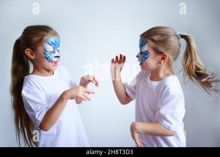 Zwei Schwesternmädchen mit Aqua-Make-up in Form eines blauen WasserTierkreiszeichens zeigen einen Tiger auf weißem Hintergrund, ein konzeptionelles Symbol des neuen 2022 Stockfoto