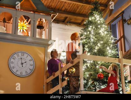 21. November 2021, Sachsen, Schkeuditz: Dietmar Sawatzke und seine Frau Martina schmücken mit ihrer neunjährigen Enkelin Alicia (l-r) einen großen Weihnachtsbaum auf der Tenne ihres vierseitigen Bauernhofes. Für den 71-jährigen ehemaligen Wirtschaftsarbeiter und seine gleichaltrige ehemalige Bankierin Martina ist Weihnachten mit seinen Ritualen der wichtigste und schönste Feiertag des Jahres. Besonders dekoriert ist die 100 Quadratmeter große Tenne, auf der der Vermieter Giebelwände mit einem Kirchturm aus von Stürmen zerstörten Verkaufszelten errichtet hat, die nun Gartenmöbel und andere verbergen Stockfoto