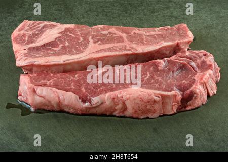 Frische rohe New Yorker Streifensteaks auf schwarzem Schneidebrett Stockfoto