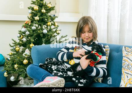 Das kleine Mädchen streichelte ihren schwarzen Welpen im Wohnzimmer beim weihnachtsbaum Stockfoto