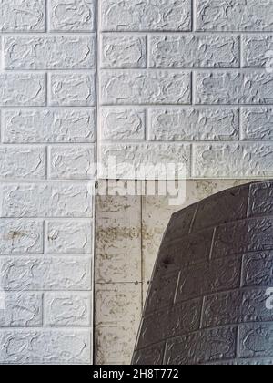 Die Tapete beginnt sich abzulösen. Die Tapete aus alten weißen Ziegeln schälte sich von der Wand im Raum, weil es feucht war oder sich nicht gut klebte. Reparieren Sie A Stockfoto